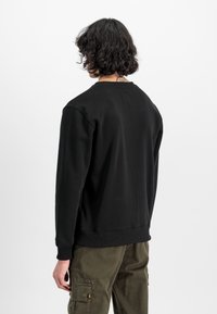 Svart hettegenser med lange ermer og rund hals. Laget av glatt stoff, har et lite merke på baksiden. Sammen med olivengrønne cargo-bukser.