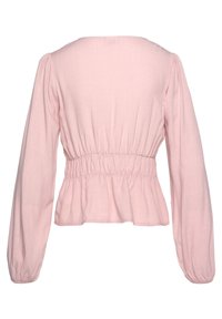 Rosa blus med långa ärmar som har en fyrkantig halsringning, rynkad midja och volangnedre del. Tillverkad av lätt tyg med en slät textur.