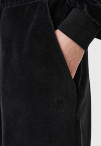 Svarta velour joggers med elastiska mudd och en sidficka, med en subtil präglad logotyp på underbenet. Mjuk textur och avslappnad passform.