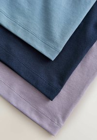 Trzy złożone koszulki w odcieniach jasnoniebieskiego, granatowego i lawendowego. Tkanina wydaje się miękka, z widocznym przeszyciem wzdłuż brzegów.
