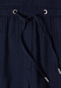 Cinturilla de pantalón de tela azul marino con textura, con elástico y cordón ajustable con terminales y ojales de metal plateado.