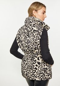 Vesta pufo cu imprimeu de leopard în nuanță bej, cu pete negre, guler înalt și talie ajustată. Purtați-o peste un top negru cu mânecă lungă.