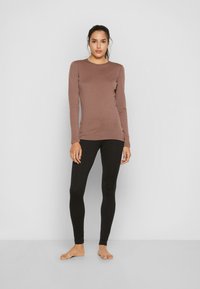 Bruin langmouw shirt met een fitted design, gecombineerd met zwarte leggings. Het shirt heeft een ronde halslijn en zachte, gladde stof.