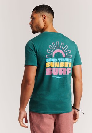 Groen katoenen T-shirt met een retro print op de achterkant met de tekst "Good Times" en een zonontwerp in roze en geel. Korte mouwen en een ronde hals.