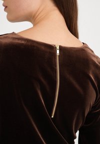 Brun sammetstop med rund halsringning och en guldfärgad dragkedjedetalj på baksidan. Texturen ser mjuk och slät ut.