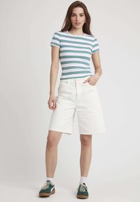 Shorts en coton blancs à coupe décontractée, avec une fermeture à bouton à l'avant et des poches latérales. Assortis à un haut à manches courtes rayé.