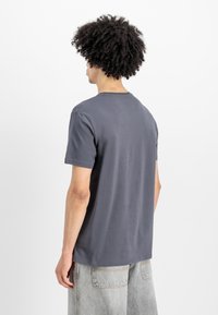 Hallhallane puuvillane t-särk ümmarguse kaelusega ja lühikeste varrukatega, millel on lõdvas stiilis ja minimalistlik kujundus, kantud heledate teksadega.