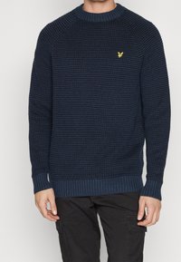 Maglione lavorato a maglia blu navy con un motivo testurizzato, colletto e polsini a coste, caratterizzato da un piccolo logo dorato sul lato sinistro del petto.