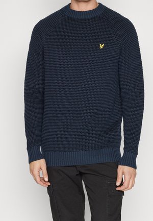 Pull en tricot bleu marine avec un motif texturé, col et poignets côtelés, doté d'un petit logo doré sur la poitrine gauche.