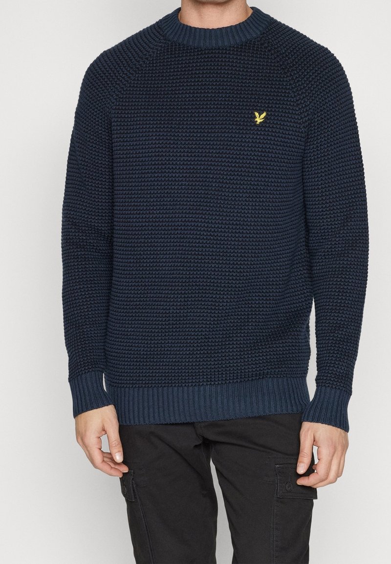 Maglione lavorato a maglia blu navy con un motivo testurizzato, colletto e polsini a coste, caratterizzato da un piccolo logo dorato sul lato sinistro del petto.
