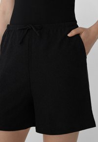 Pantaloni corti neri in tessuto testurizzato con vita elasticizzata e cordoncino, dotati di tasche laterali e vestibilità ampia.