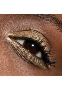 Close-up of an eye featuring gold metallic eyeshadow, dark lashes, and a smooth, warm skin texture in a rich brown hue.