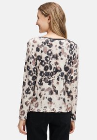 Lange mouwtop in lichtbeige met een zwart en bruin luipaardprint. De stof lijkt zacht met een licht gestructureerde afwerking. Heeft een ronde halslijn.