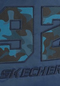 Tela de marinero con un audaz patrón de camuflaje en azul y negro. Presenta el logo de "SKECHERS" y un gran número "92" en aplicación texturizada.