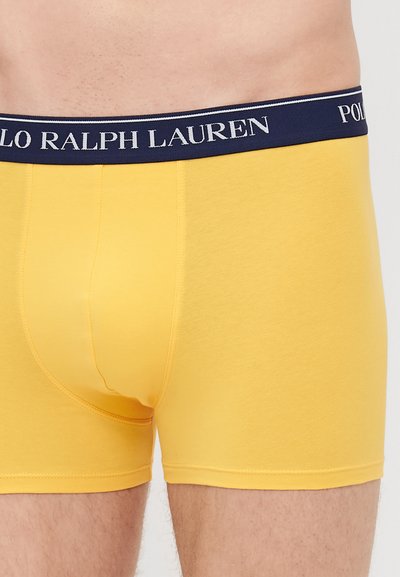 Rumene bombažne bokserice z mornarsko modrim pasom, ki vsebuje belo blagovno znamko "POLO RALPH LAUREN". Gladka tekstura in prilegajoča se zasnova.