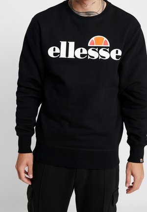 Man in een zwarte sweatshirt met een wit en oranje "ellesse" logo op de borst en bijpassende zwarte broek met zijzakken.