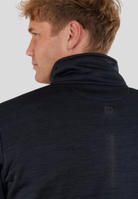 Dark gray zip-up jacket with a high collar, textured fabric, subtle logo detail, and reflective strip on the back.
