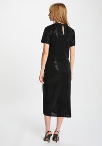 Completo a due pezzi nero con paillettes, composto da una maglietta a maniche corte con apertura a chiave sul retro e una gonna midi coordinata. Tacchi completano il look.