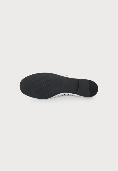 Semelle en caoutchouc noire d'une chaussure blanche avec une prise texturée sur les orteils et le talon sur fond blanc.