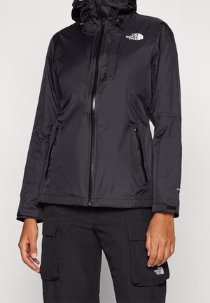 Musta hupullinen North Face -takki, jossa etuvetoketju ja vetoketjulliset sivutaskut, yhdistetty mustiin cargo-housuihin, joissa on läppätaskut.