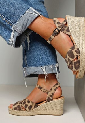Luipaardprint wedge sandalen met een jute touwzool, enkelbandjes met een gesp, gecombineerd met versleten spijkerbroeken.