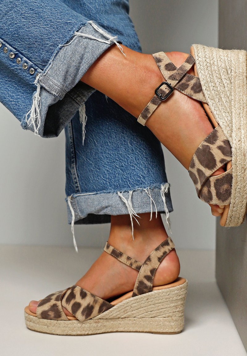 Leopard print wedge sandals with a jute rope sole, ankle straps with a buckle, paired with distressed denim jeans.