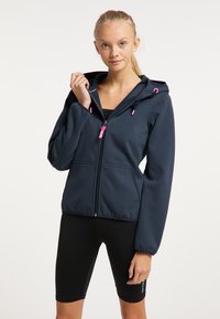 Felpa con zip blu navy con dettagli rosa sulla zip e sui lacci, presenta tasche laterali e un taglio comodo. Indossata sopra pantaloni da bici neri.