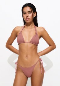Bikini rose avec un col licou et des bonnets triangulaires, en tissu texturé et avec des liens sur les côtés du bas pour un ajustement réglable.