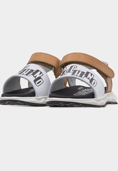 Παιδικά σανδάλια με ανοιχτά δάχτυλα, καφέ λουριά στον αστράγαλο και λευκά μπροστινά λουριά με μαύρο γραφικό κείμενο σε υφασμένα πατούσια από καουτσούκ.