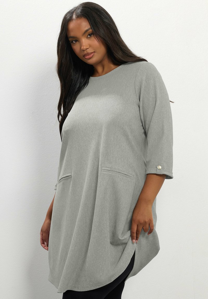 Tunic grigia con maniche a tre quarti, morbida texture a coste, tasche laterali e orlo arrotondato. Dettagli con bottoni sulle maniche.