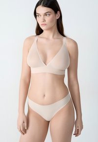 Bralette beige douce avec une forme triangulaire et une large bande, assortie à des culottes de bikini lisses et coordonnées. Fabriquée en matériau léger et extensible.