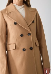 Bruin wollen dubbelbreasted jas met grote zwarte knopen, pieklapels en zijzakken. Zachte textuur en op maat gemaakt ontwerp.