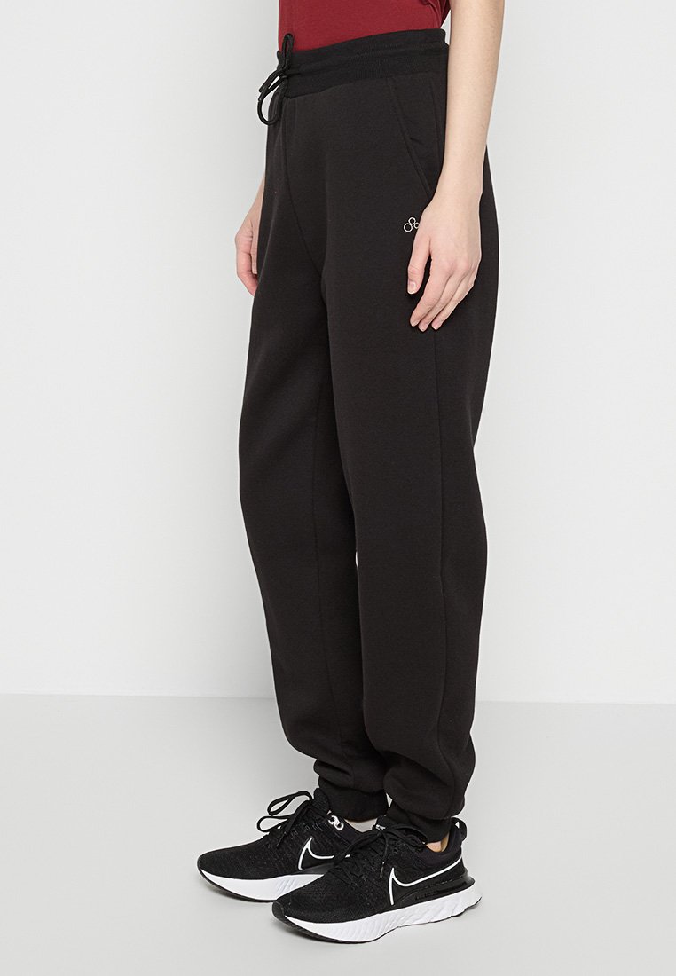 Pantalons de survêtement noirs en tissu doux, avec une taille à cordon de serrage, des poches latérales et un petit logo près de la hanche.