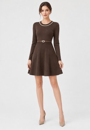 Donna che indossa un vestito marrone a maniche lunghe a linea ad A con dettaglio collana di perle e cintura abbinata, abbinato a tacchi alti beige, in piedi dritta.