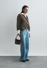 Cămașă maro cu carouri și guler alb, blugi largi albaștri cu un model cu puncte, pantofi negri și o poșetă mică maro.