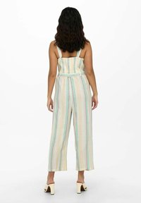 Combinaison rayée en tissu léger, présentant des couleurs pastel, des jambes larges, des bretelles au dos et une taille cintrée avec un détail ceinture.