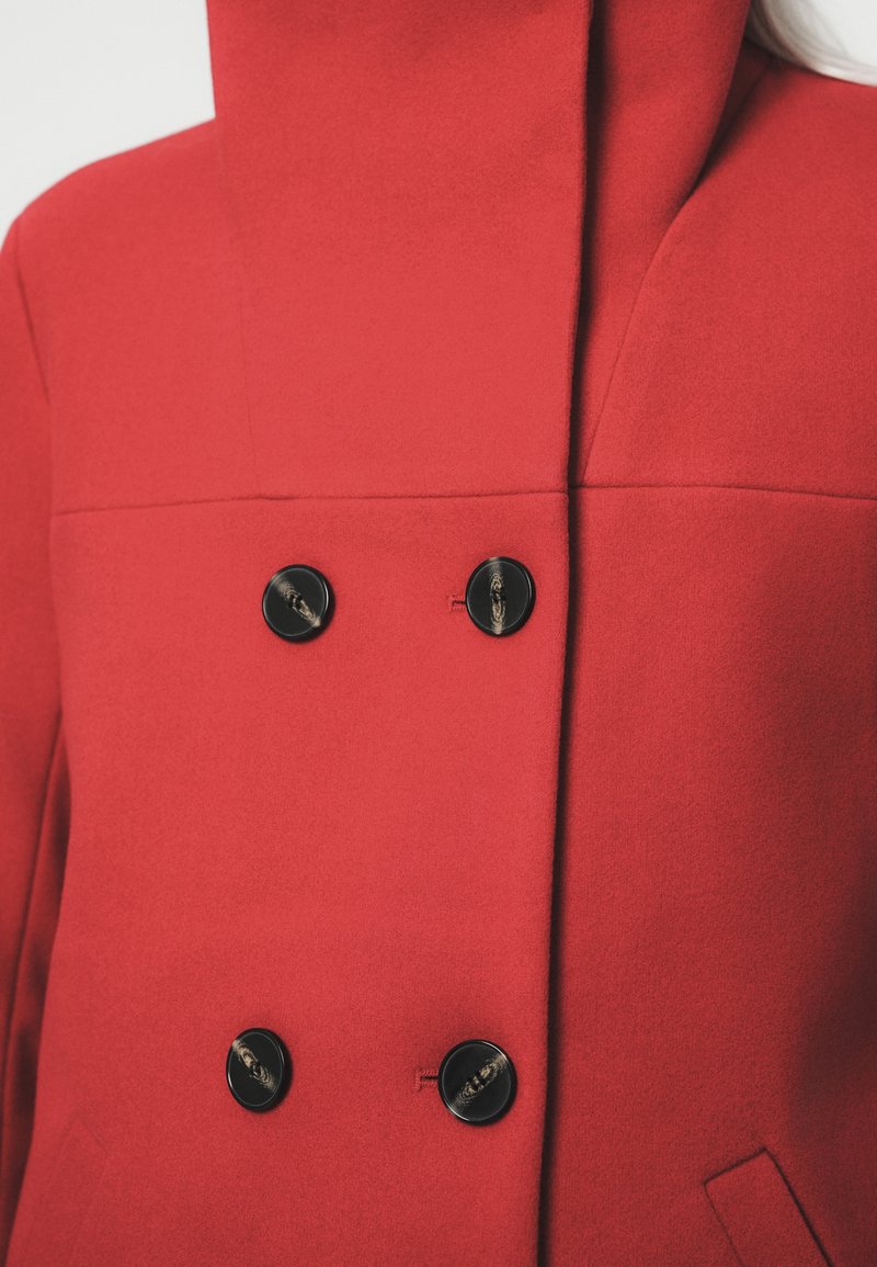 Roter Wollmantel mit hohem Kragen, doppelt knöpfbarer Ausführung mit zwei schwarzen Knöpfen und glatter Textur sowie minimalen Nähdetails.