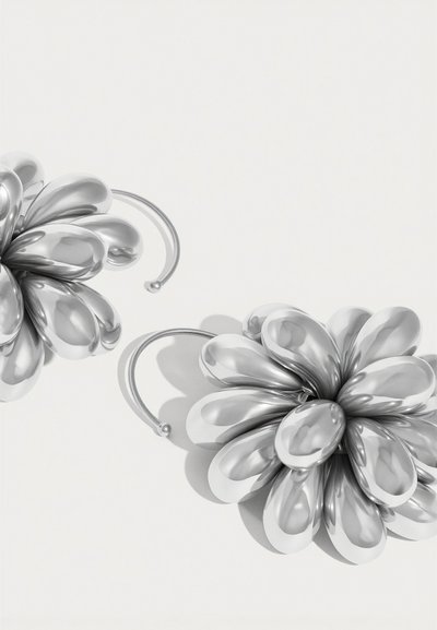 Ασημένια σκουλαρίκια σε σχήμα λουλουδιού με στρογγυλεμένα πέταλα, λεία υφή και καμπύλο σχέδιο γάντζου. Η αντανακλαστική επιφάνεια ενισχύει το βάθος και τις λεπτομέρειες.