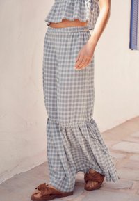 Lys blå og hvid ternet maxi-skjørt med en bølget kant, parret med brune sandaler. Stoffet ser blødt og let ud.