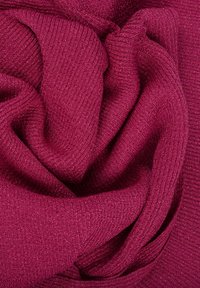 Tissu tricoté doux, plié, de couleur magenta foncé avec une texture côtelée visible et de fines fibres, créant des courbes douces et des ombres.
