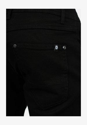 Jeans in denim nero con una tasca posteriore dotata di etichetta logo, rivetti metallici e cuciture a contrasto. Texture liscia e design aderente.