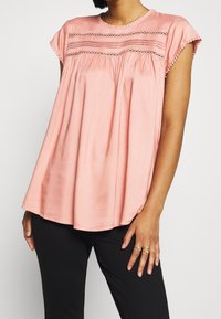Top rosa a maniche corte con un design arricciato, caratterizzato da ricami orizzontali e un colletto testurizzato. Abbinato a pantaloni neri.