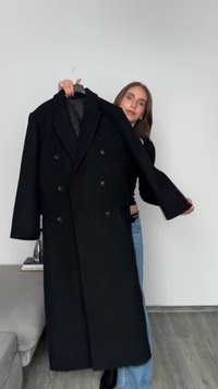 Μαύρο διπλό παλτό με γιακά με εγκοπές, μεγάλα κουμπιά και μακριά μανίκια. Λείο ύφασμα και εφαρμοστό σχέδιο, κρεμασμένο σε κρεμάστρα.