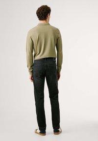 Polo de manga larga en color oliva claro combinado con jeans oscuros. Los jeans tienen un corte recto y dos bolsillos traseros. Zapatillas blancas casuales con acentos en azul.