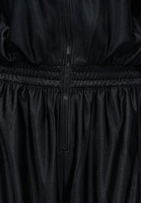 Juodas tekstūruotas audinio aprangos artimas planas su vertikaliu užtrauktuku ir elastiniu liemens juostos dekoru centre.