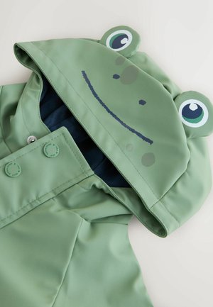 Grön vattentät regnrock med en groddesign med ögon och ett leende. Tryckknappar och ett fodrat inre i mörkblått.