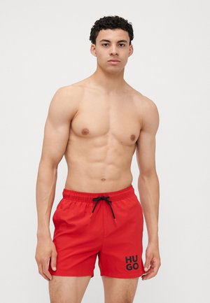 Pantaloni da bagno rossi con cintura elastica, coulisse nera e logo "HUGO" in nero sul lato destro inferiore. Tessuto liscio e leggero.
