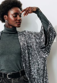 Kimono en sequins argentés avec des manches larges sur un col roulé gris. Accompagné de jeans en denim noir et d'une boucle d'oreille statement. Texture douce, apparence scintillante.