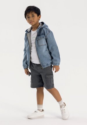 Veste en denim avec capuche grise, t-shirt blanc, shorts cargo gris et baskets blanches. Comprend des détails avec des poches avant et des poignets élastiques.
