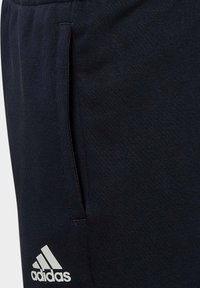 Pantaloni sportivi neri con una texture morbida, dotati di tasche laterali e un logo Adidas bianco vicino all'orlo. Inclusa una vita regolabile.
